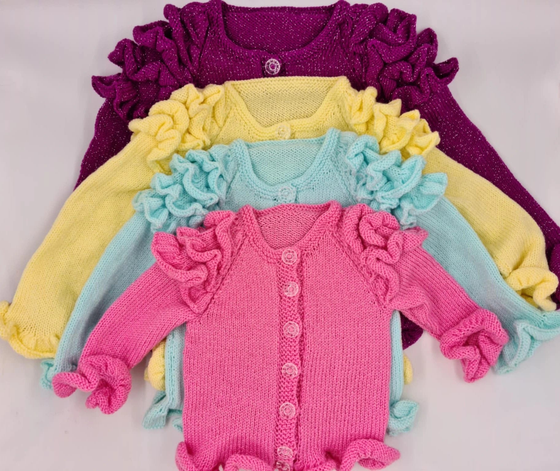 Stack of colorful children's cardigans with ruffled details on a light gray background