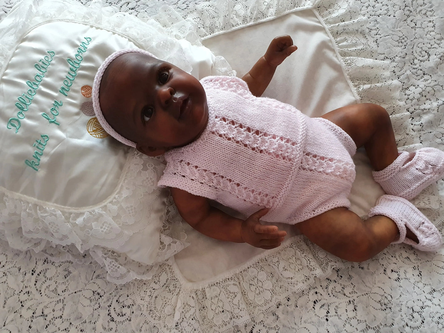 Baby doll in a pink outfit lying on a textured surface with embroidered text.