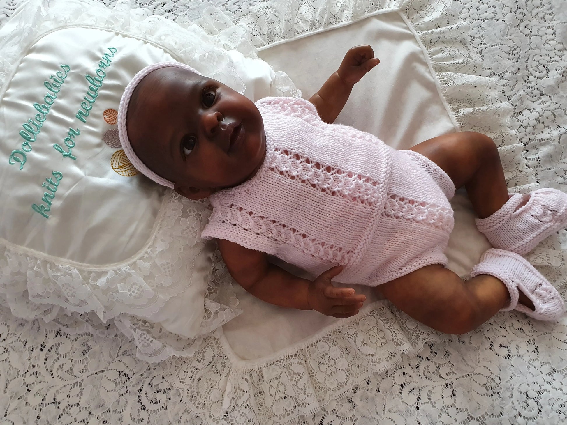 Baby doll in a pink outfit lying on a textured surface with embroidered text.