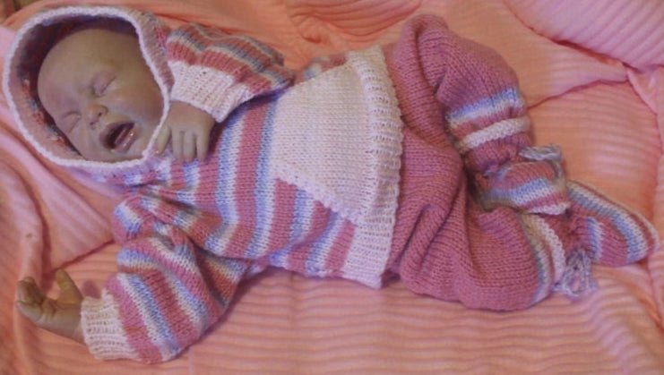 Baby doll in a pink and white striped outfit on a pink blanket
